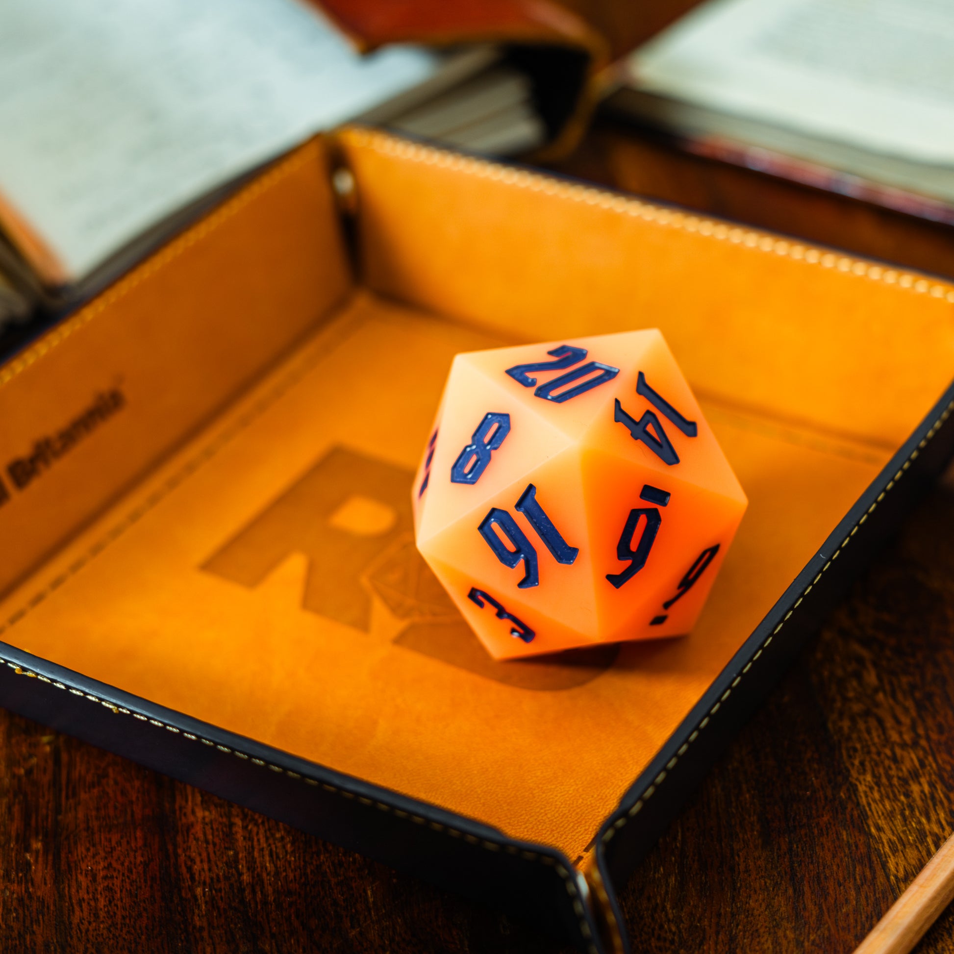 Roll Britannia Orange Bouncy Silicon 55mm D20 Glow in the Dark Dungeons and Dragons Dice on branded leather dice tray